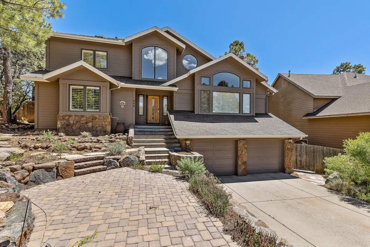The home's inviting exterior, marked by a welcoming front door, large windows, and landscaped steps, creates a sense of arrival. Families and groups can be seen gathering or strolling, suggesting a transition point between the serenity of the retreat and the activities that lie just minutes away in downtown Flagstaff.