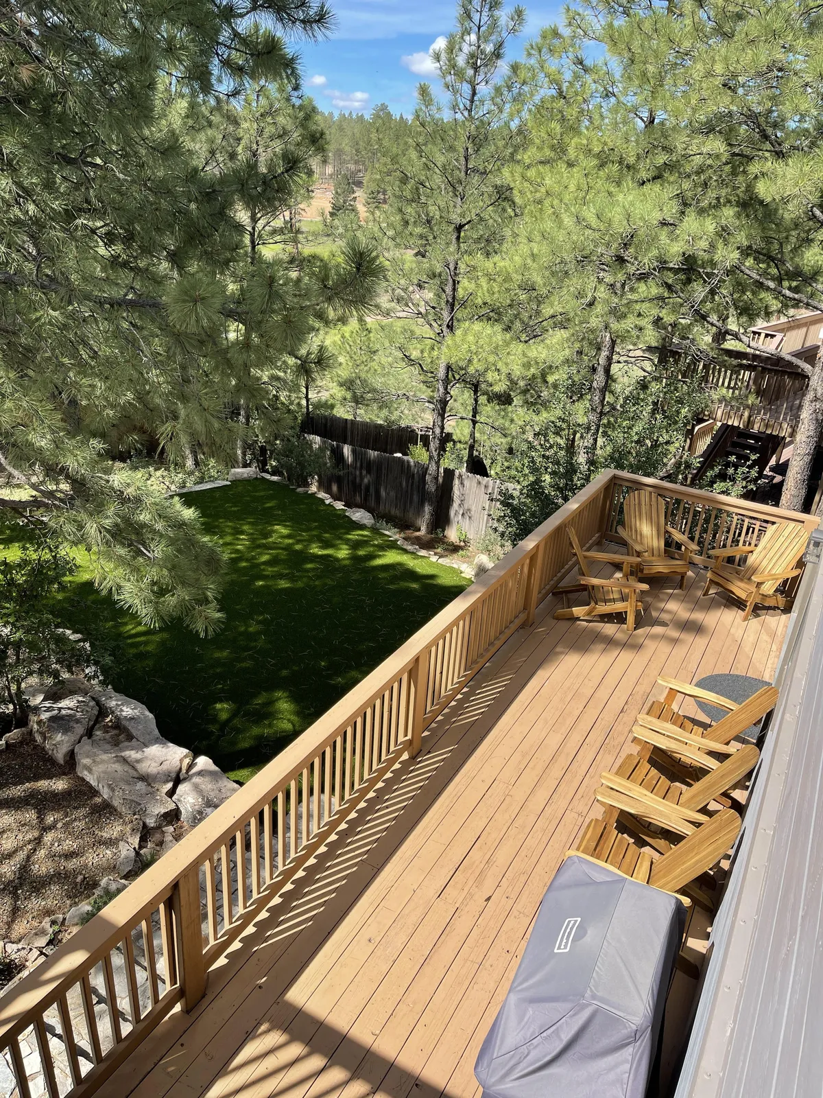 This inviting exterior shows a deck furnished with chairs overlooking a lawn and framed by trees. It evokes peaceful moments like morning coffee or stargazing, with clear cues of a space designed for gathering, reflection, and connecting with nature throughout the changing seasons.