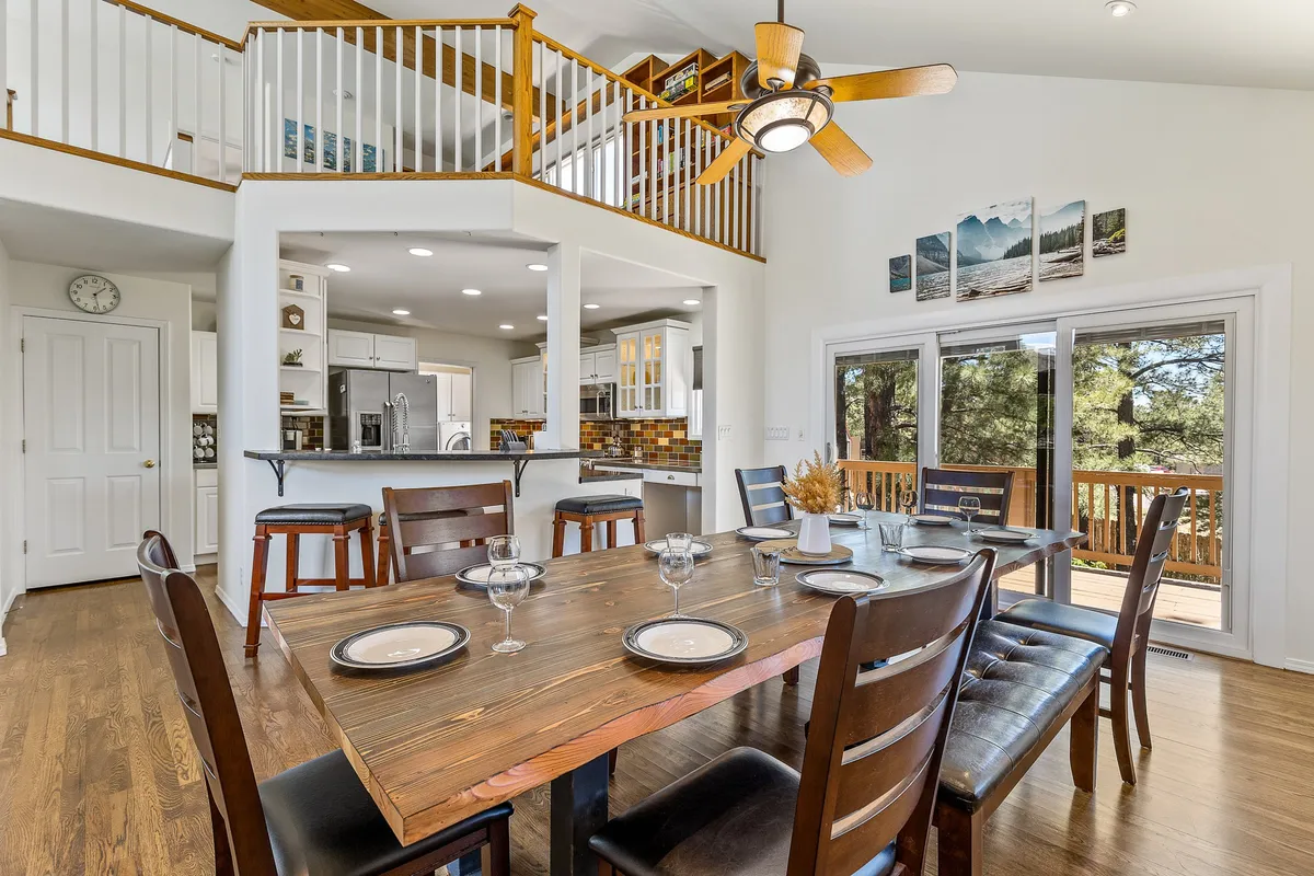 An inviting open-plan dining area featuring a large dining table, adjacent open kitchen, and windows looking out onto the landscape. The space exudes warmth and is ideal for shared meals, entertaining guests, and enjoying the views while dining together.