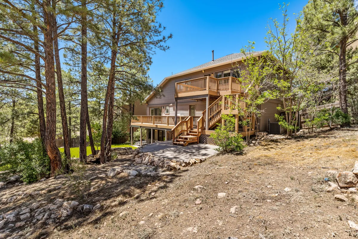 This exterior image captures the wooden deck surrounded by towering pines, with large windows facing out into the forest. The setting suggests tranquility and connection to nature, ideal for relaxing outdoors or enjoying a meal with family. The image radiates a relaxed atmosphere, enhanced by the soft hues of sunset and the lush green forest.