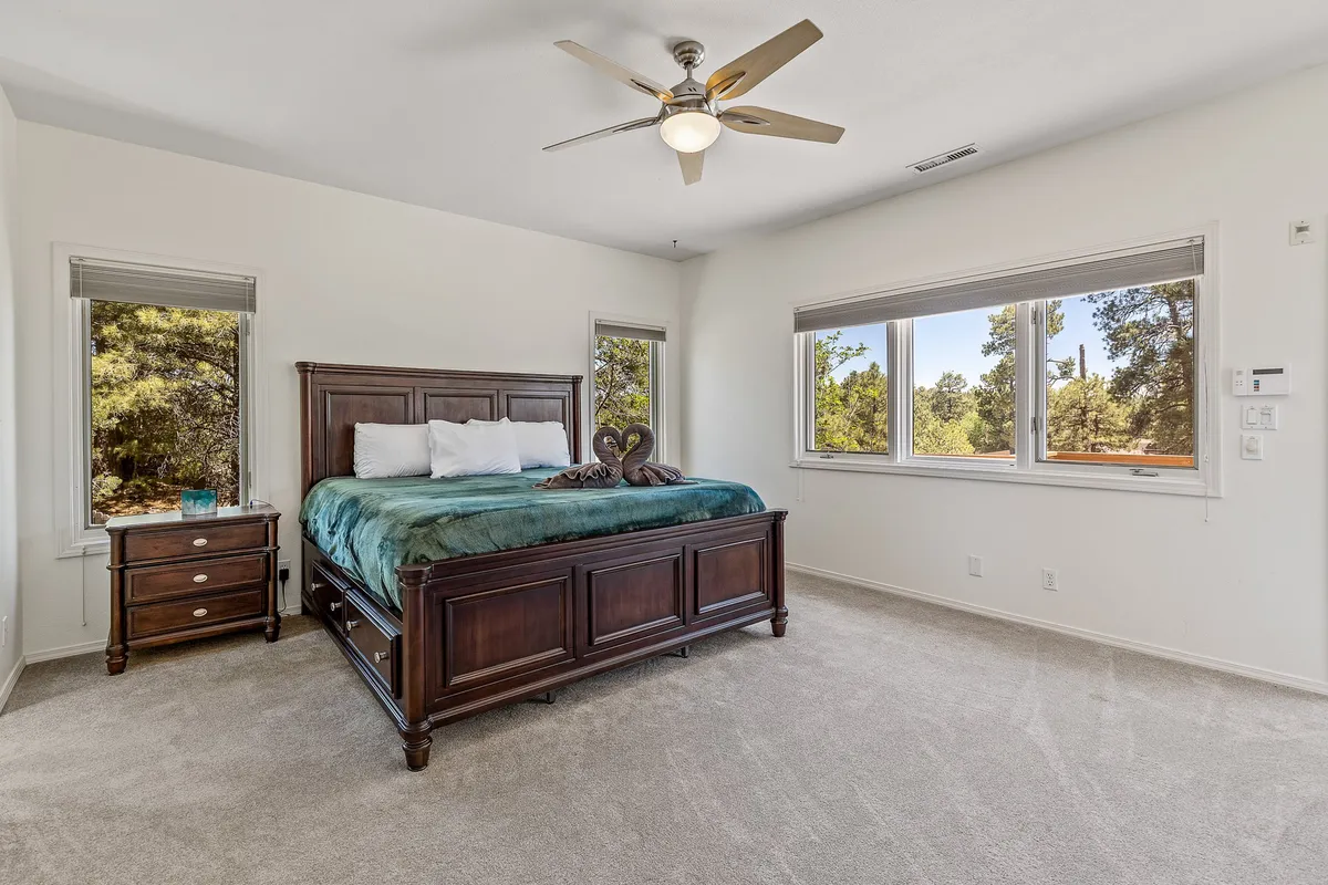 A tranquil bedroom featuring a king-sized bed dressed in soft linens, set beside large windows that offer views of the surrounding trees. A nightstand sits nearby, and the room is filled with natural light, giving it a restful, inviting atmosphere.