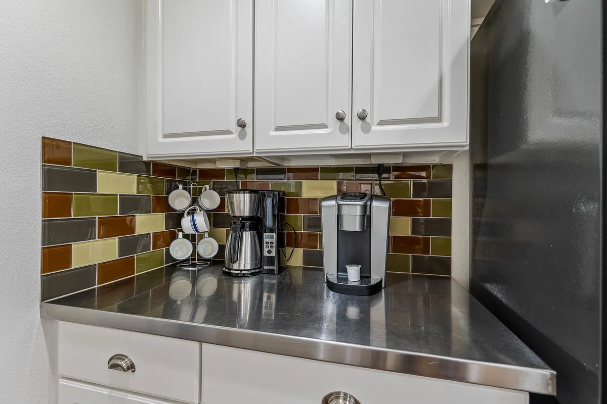 This image focuses on a cozy coffee station with a coffee maker and colorful backsplash, emphasizing the role of coffee and casual moments in the kitchen. The setting is intimate and functional, inviting guests to enjoy morning rituals or dessert.