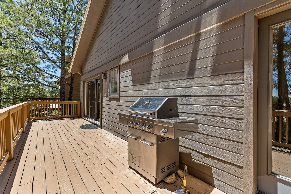 A spacious deck with a grill, surrounded by lush trees, offers outdoor seating and relaxation. The setting is inviting, with plenty of room for people and pets to enjoy fresh air after a day of exploring the mountain trails together.