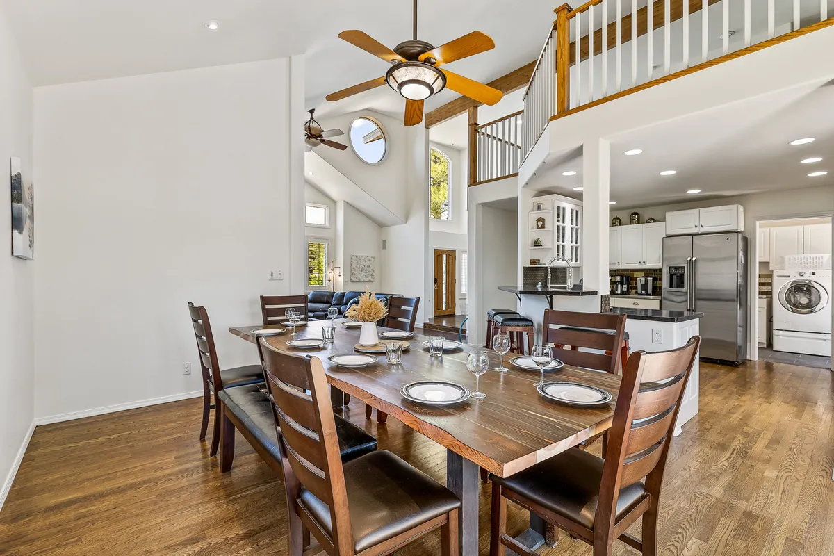 A warm, welcoming dining area is pictured here, featuring a dining table set near large windows that flood the space with natural light. The kitchen area is visible, reinforcing the close connection between cooking and dining.