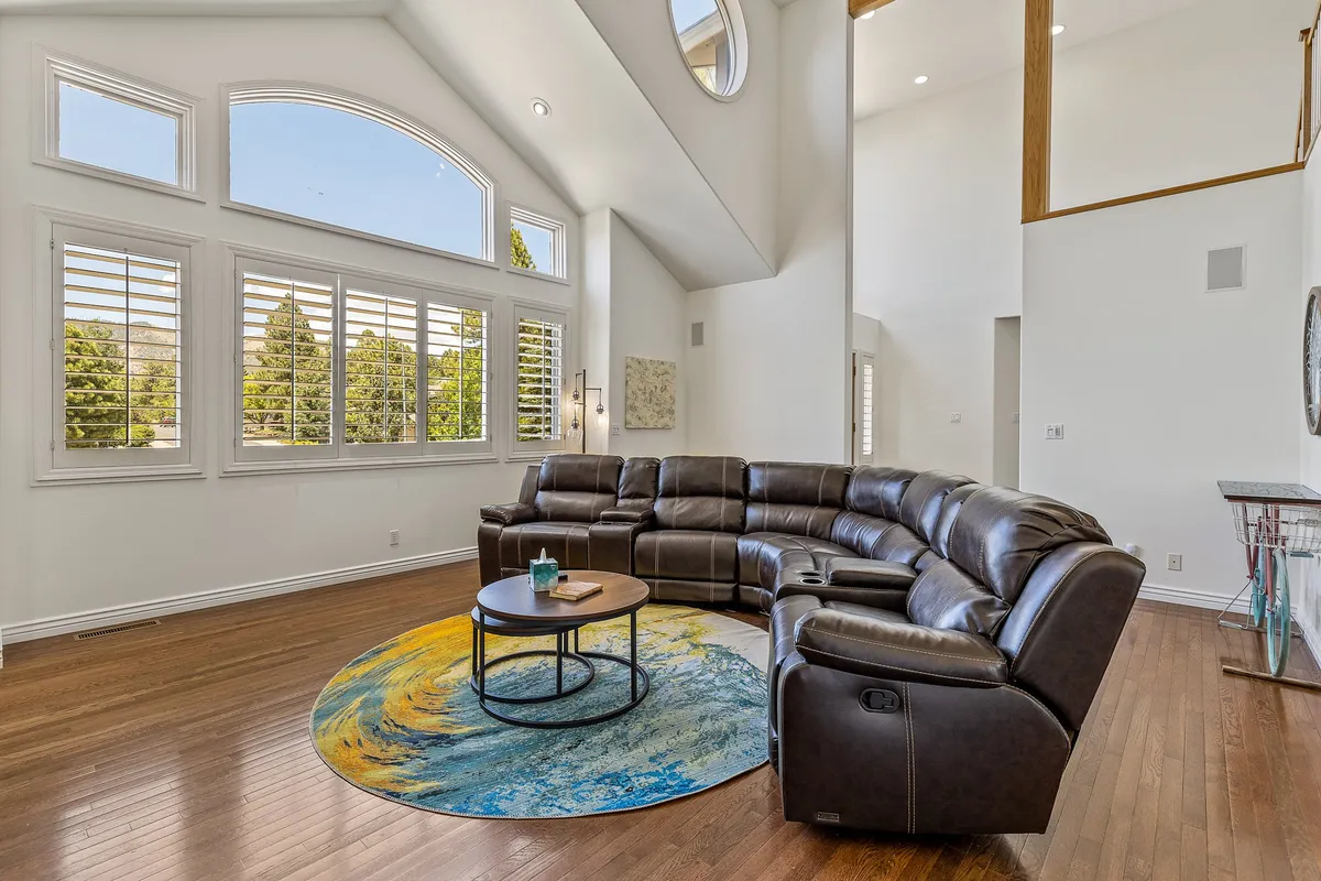 A spacious living area with a large sectional sofa, a vibrant area rug, and wide windows that frame views of trees and natural light. The seating area is arranged for easy conversation or relaxation, creating an inviting atmosphere for groups to connect.