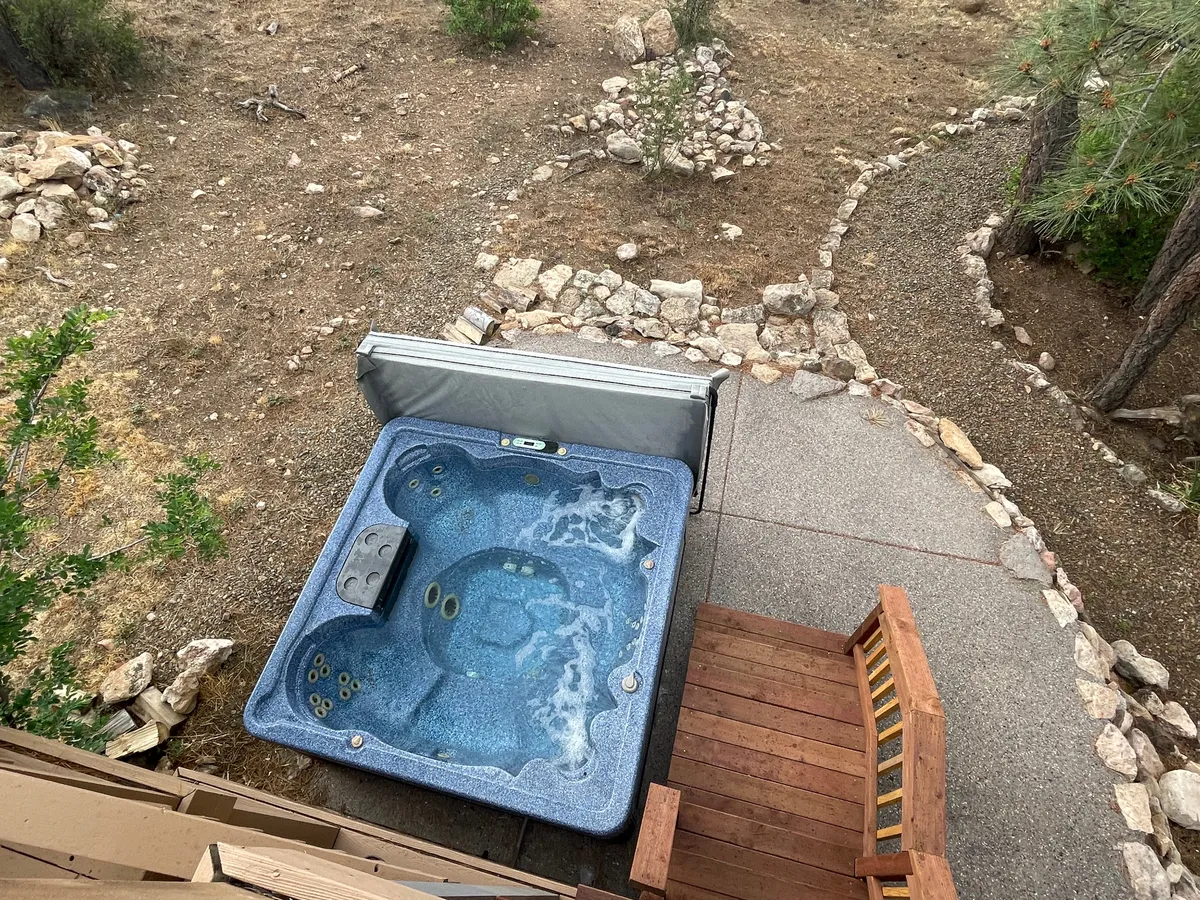 A tranquil outdoor area featuring a hot tub, wooden bench, and stone pathway nestled in a natural landscape. The setting evokes relaxation and peacefulness, ideal for unwinding under the stars or after outdoor excursions.