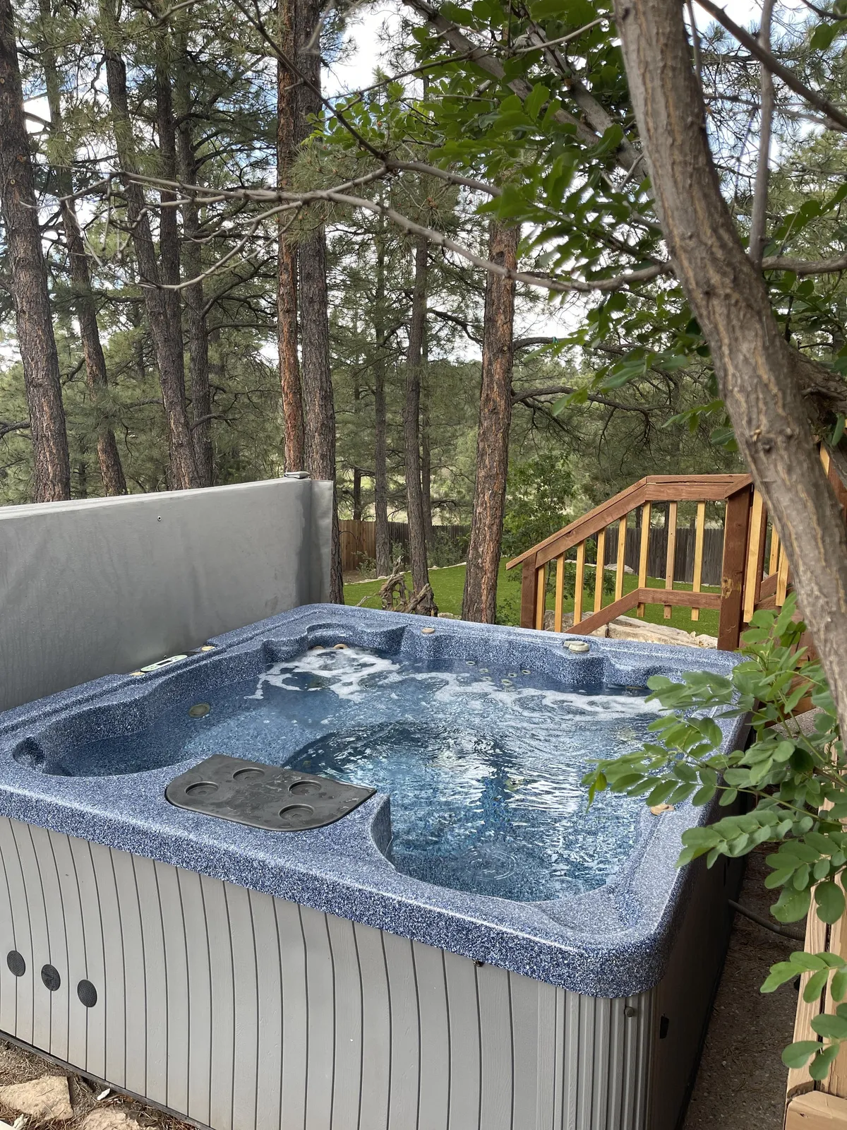 A serene hot tub set among surrounding trees with wooden steps leading up to it, evoking a sense of relaxation after outdoor adventures. The natural setting suggests both privacy and a strong connection with the outdoors.