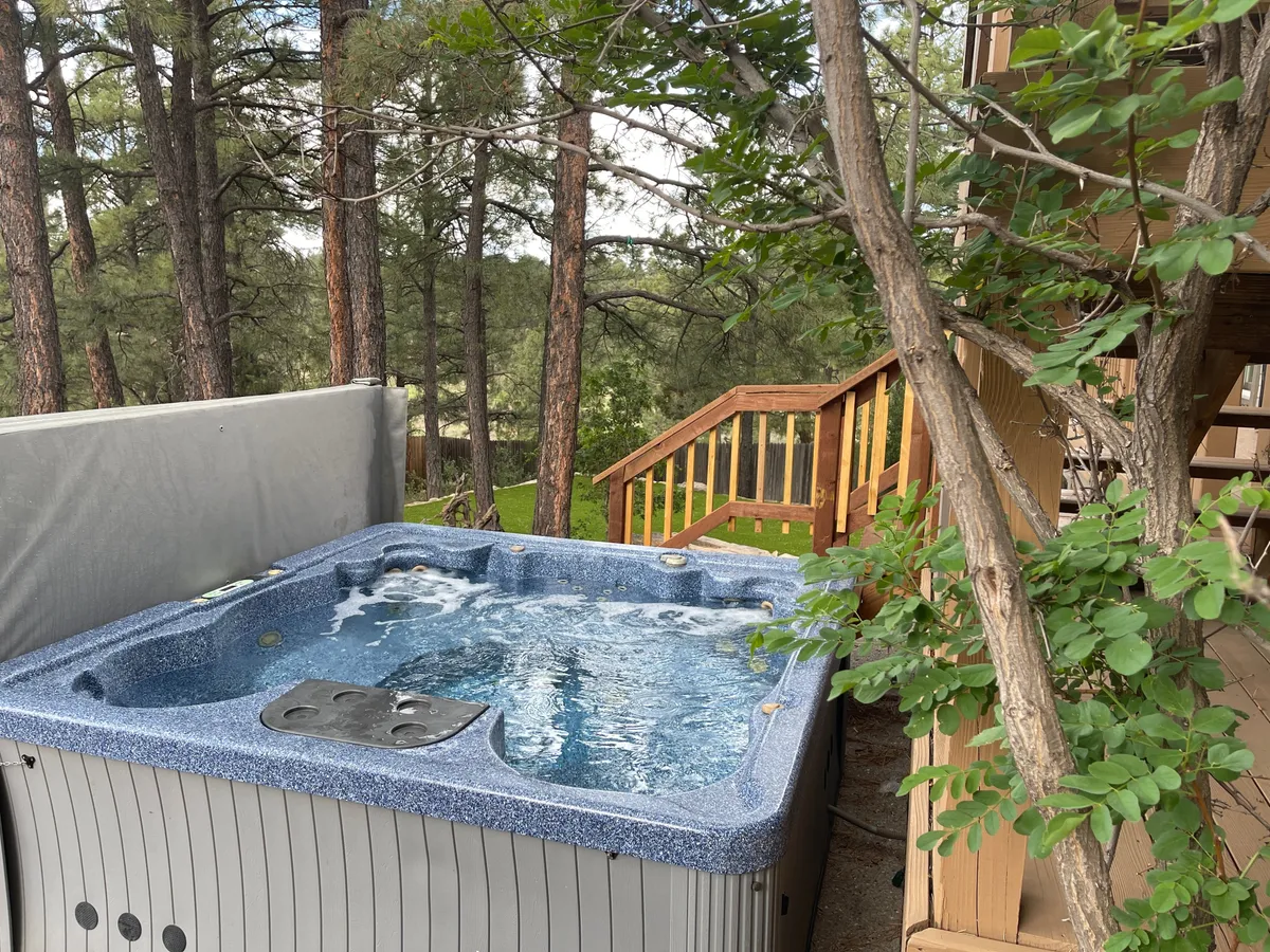 This exterior image showcases a private hot tub nestled on a wooden deck surrounded by trees, with the gentle light suggesting the possibility of both daytime relaxation and evening stargazing. The natural setting emphasizes tranquility and connection to the outdoors.