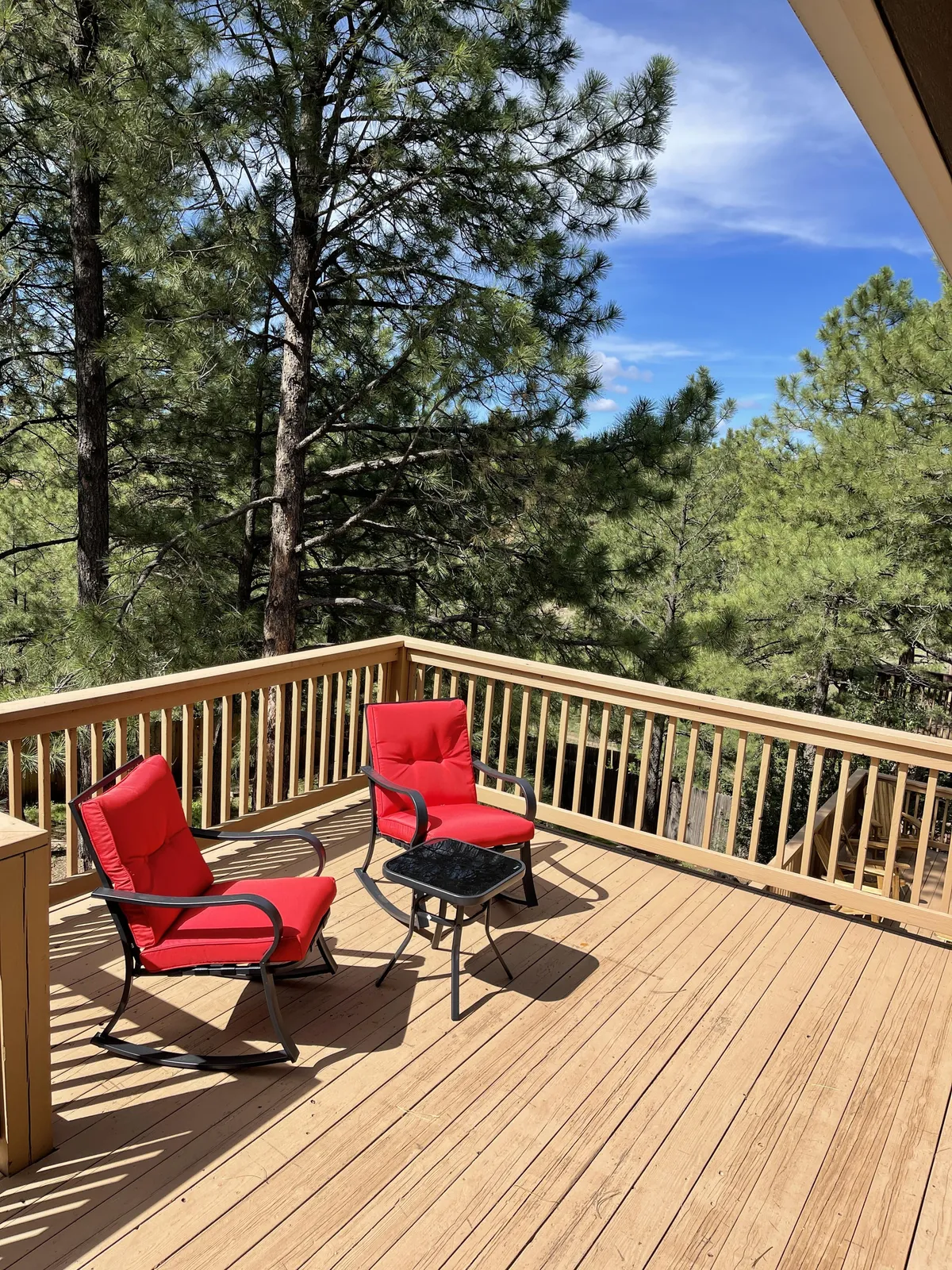 Two bright red chairs and a small black table sit beneath the trees, providing a cozy nook for morning coffee or evening relaxation. The surrounding forest is lush, and the open sky above hints at the pristine stargazing opportunities of Flagstaff’s Dark Sky City status.