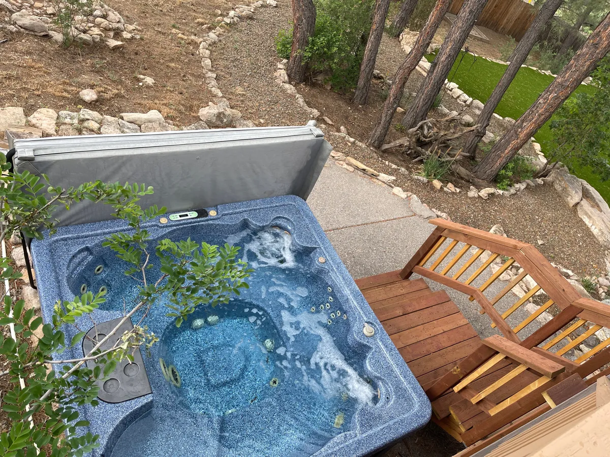 A private hot tub nestles among greenery beside wooden stairs, inviting guests to soak and relax after a day of outdoor adventure. The tranquil surroundings and natural setting highlight the luxury and restorative qualities of the retreat, especially appealing during cooler evenings or after winter activities.