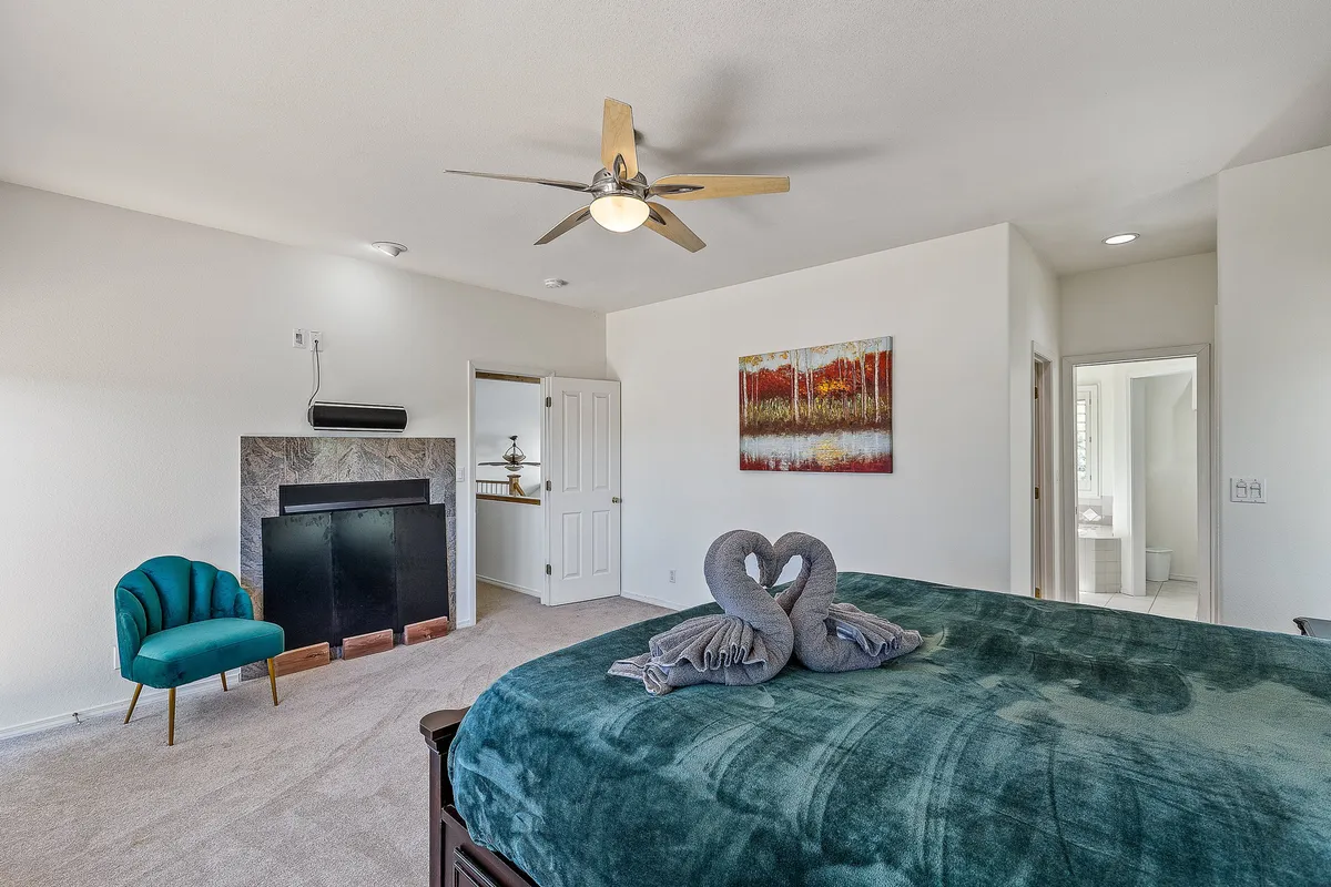 A cozy bedroom with a bed adorned with decorative swan towels, artwork on the wall, an accent chair, and a fireplace. The space feels intimate, romantic, and thoughtfully designed for relaxation.