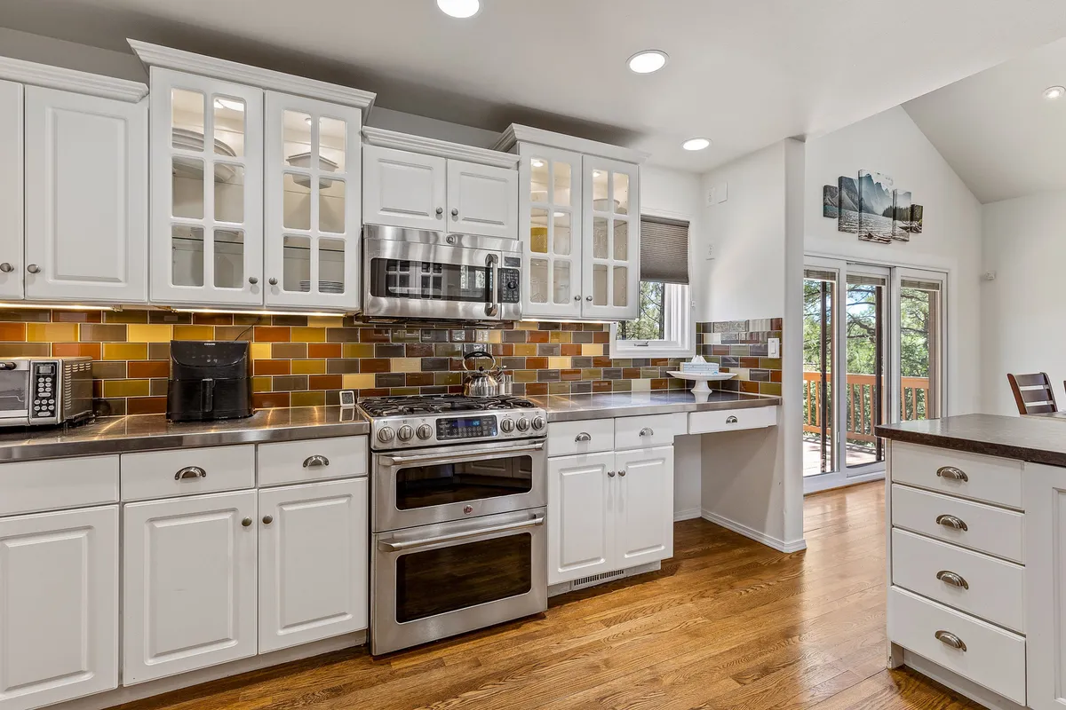 This image highlights a modern kitchen with stainless steel appliances, a colorful backsplash, and white cabinetry. The space looks bright and functional, ideal for cooking and entertaining, perfectly showcasing the 'gourmet' aspect described in the section.